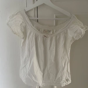 Vit blus från Odd Molly - Söt vit blus från Odd Molly med bred smockad kant vid halsringningen och korta puffärmar. Blusen har en luftig och romantisk känsla, perfekt för varma dagar. Dekorativ etikett i nederkanten med Odd Mollys signaturtext.
