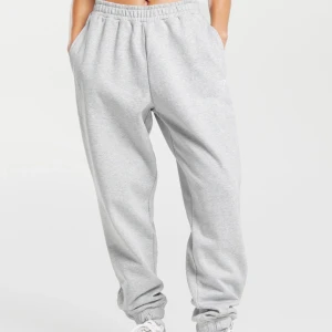 Grå mjukisbyxor från Gymshark - Säljer ett par klassiska grå mjukisbyxor från Gymshark i storlek S. Byxorna har sidofickor och en liten vit Gymshark-logga på ena benet. Perfekta för en avslappnad stil. Säljer för att de är lite för stora, har bara använts en gång. Originalpris: 450 kr