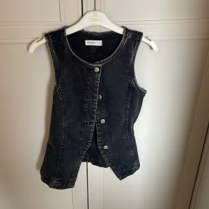 Svart jeansväst från Gina Tricot - Cool svart jeansväst från Gina Tricot med knappar framtill. Västen har en klassisk rak passform och är ärmlös, perfekt att styla över en t-shirt eller skjorta för en trendig look🌟🌟