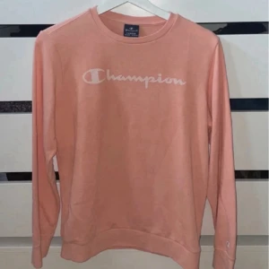 Ljusrosa sweatshirt från Champion - Säljer en ljusrosa sweatshirt från Champion i storlek XL i barnstorlek=13-14 år. Tröjan har rund halsringning, långa ärmar och vit logotyp framtill. Perfekt för en avslappnad och sportig stil.
