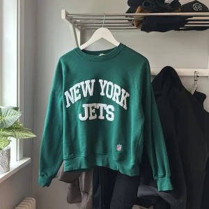 Grön New York Jets sweatshirt från H&M - Mörkgrön sweatshirt med vit text 'NEW YORK JETS' framtill. Rund halsringning och ribbade muddar vid ärmslut och nederkant. Officiell NFL-logga nertill. Perfekt för sportiga outfits. Fint skick 🥰