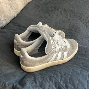 Gråa Addidas campus storlek 39 - Snygga grå sneakers från Adidas campus i mocka med klassiska vita ränder och snörning. Perfekta för en avslappnad stil. skriv för fler frågor eller bilder.