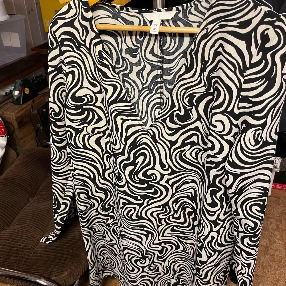 Säljer en stilren svartvit blus från H&M med ett unikt abstrakt mönster. Blusen har långa ärmar och en rund halsringning. Perfekt för att ge din outfit en modern touch. 🖤🤍. Neuletakit & Villapaidat.