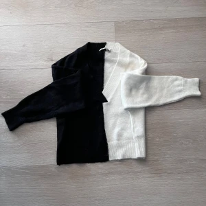 Svartvit stickad tröja - Unik stickad tröja i svart och vitt med delad design. Ena sidan och ärmen är svart, andra sidan och ärmen är vit. Tröjan har rund hals och långa ärmar. Perfekt för dig som vill sticka ut med en cool och trendig look.