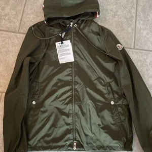 Moncler Windbreaker - Säljer en snygg grön windbreaker från Moncler med huva och dragkedja framtill. Jackan har två fickor med knappar och Moncler logga på armen. Kvitto kommer med. Priset är inte hugget i sten.
