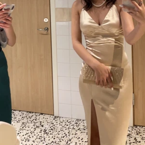 Champagnefärgad balklänning  - Säljer min balklänning champagnefärgad satin med smala korsade axelband i ryggen och djup v-ringning. Klänningen har en hög slits framtill och figurnära passform. Är dock lite nopprig ovanför sliten. Jag är 162cm lång.