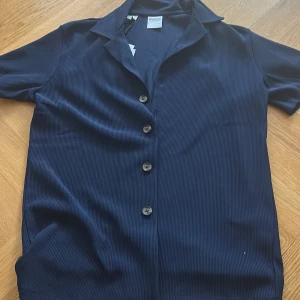 Mörkblå kortärmad skjorta från Selected Homme - Säljer en helt ny (lappen kvar) stilren mörkblå skjorta från Selected Homme. Skjortan har korta ärmar, klassisk krage och knäppning framtill med fyra knappar. Perfekt för en avslappnad men snygg look. Storlek S/M