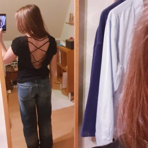 Svart topp med öppen rygg och snörning från Panos Emporio - Svart topp med djup öppen rygg och snygga korsade snören. Kortärmad och tillverkad i en mjuk blandning av polyester och viskos. Perfekt för dig som vill ha en stilren men ändå unik look. Funkar både till vardags men även träning! Aldrig använd.