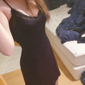 Svart slipklänning med spets från Le Chateau - Svart slipklänning från Le Chateau med tunna axelband och spetsdetaljer längs urringningen. Klänningen har en enkel, rak passform och är tillverkad i ett mjukt, lätt material som ger en elegant känsla.