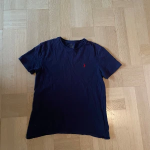 Mörkblå t-shirt från Polo Ralph Lauren - Säljer en mörkblå t-shirt från Polo Ralph Lauren med klassisk röd broderad logga på bröstet. Enda defekten på t-shirten kan man se på sista bilden. Passar S/M, priset kan diskuteras. 