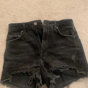 Svarta jeansshorts från Zara - Snygga svarta jeansshorts från Zara med fransig kant och slitna detaljer. Klassisk femficksmodell med hög midja och råa benslut. Perfekta för en avslappnad stil.