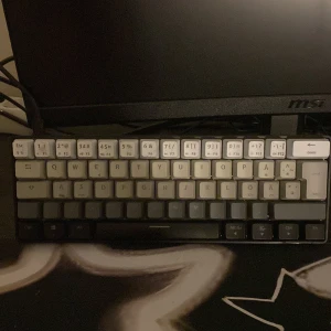 Mekaniskt tangentbord med nordisk layout NOS - Säljer ett kompakt mekaniskt tangentbord med nordisk layout. Fading colour. Tangenterna är i olika nyanser av vitt, grått och svart. Tangentbordet har låg profil och ansluts med kabel. Perfekt för gaming eller skolarbete. 65%