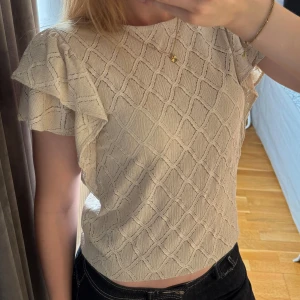 Beige blus med volangärmar från Holly & Whyte - Säljer en beige blus från Holly & Whyte (köpt på Kappahl) med strukturmönster och volangdetaljer på ärmarna. Toppen är i storlek S och köptes förra året. Super söt men aldrig använd och därför säljer jag den nu. Hör av dig vid frågor🫶🏽☺️