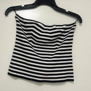 Svartvit randig ribbad tubtopp - Säljer en svartvit randig tubtopp i ribbat material. Toppen är ärmlös och har en croppad passform, perfekt för varma dagar. Klassisk och stilren design med horisontella ränder.