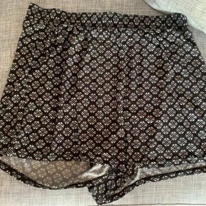 Svartvita mönstrade shorts - Svarta shorts med vitt geometriskt mönster. Lätt och luftig modell med resår i midjan, perfekta för varma dagar. Tillverkade i mjuk polyesterblandning som känns skön mot huden.