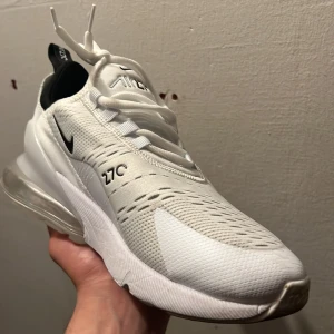 Nike Air Max 270 vita sneakers - Säljer ett par vita Nike Air Max 270 sneakers med svart swoosh och detaljer. Skorna har en luftig mesh-överdel, synlig Air Max-dämpning i hälen och klassisk snörning. Perfekta för dig som gillar sportig och modern stil. SKICKA IVÄG PRISFÖRSLAG VID INTRESSE…..
