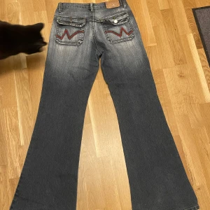 Mörkblå bootcut jeans y2k - Säljer ett par mörkblå bootcut jeans från blessing med röda broderade detaljer på bakfickorna. Jeansen har hög midja, stora framfickor och klassisk femficksdesign. Perfekta för dig som gillar en retrostil med breda ben. Midjemått: 37 cm innerbenslängd:78 cm . #y2k #y2kjeans
