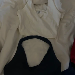 Vita och marinblå croppade linnetoppar från Brandy Melville - Två croppade linnetoppar från Brandy Melville, en vit och en marinblå. Båda har djup v-ringning och breda axelband. Perfekta att styla med jeans eller kjol för en enkel och snygg look.