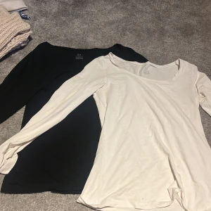 Svart och vit långärmad topp från KappAhl - Två långärmade toppar från KappAhl i storlek XS, en svart och en vit. Båda är tillverkade i mjuk ekologisk bomull och har en klassisk, rund halsringning. Perfekta basplagg till garderoben. Båda är smått genomskinliga 