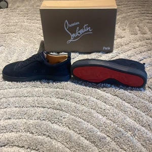 Svarta sneakers från Christian Louboutin - Säljer ett par svarta sneakers från Christian Louboutin med klassisk röd sula. Skorna är i mocka och har diskret broderad logga på sidan. Snygg och stilren design med rund tå och platt sula. De är storlek 38 men de är stora i storleken de kan passa 39 och 40