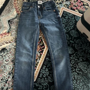 Blå jeans från Lager 157 - Säljer ett par klassiska blå jeans från Lager 157 med raka ben och normal passform. Jeansen har fem fickor, bälteshällor och knappgylf. Perfekta för en avslappnad stil. För barn runt 8-9 år gammal.