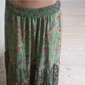 Grön blommig långkjol - Säljer en grön långkjol med blommigt mönster och resår i midjan. Kjolen har en luftig och flowy passform, perfekt för varma dagar. Materialet känns lätt och bekvämt mot huden. Passar xs-l då den är stretchig. 