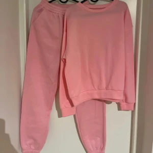 Rosa mjukisbyxor med resår - Säljer ett par ljusrosa mjukisbyxor med resår i midjan och vid bensluten. Byxorna är i en mjuk och skön bomullsblandning, perfekta för en avslappnad stil. Matchar med en likadan tröja för en hel look. Fläckar baktill vid benen som jag inte lyckats få bort 