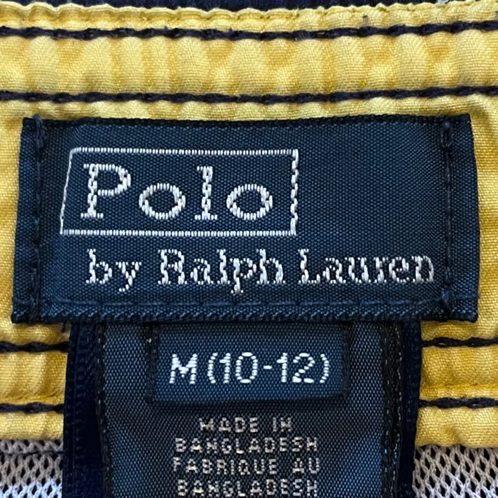 Snygga marinblå badshorts från Polo Ralph Lauren med röd broderad logga på benet och röd snörning i midjan. Klassisk modell med normal passform, perfekt för sommaren. Tillverkade i polyester för snabb torkning. Storlek: M (10-12). Hör av dig vid frågor!. Muu.