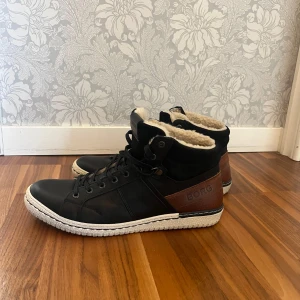 Svarta skor från Björn Borg - Snygga svarta sneakers från Björn Borg med bruna detaljer och vit sula. Skorna har snörning, rund tå och är fodrade med mjukt, ljust foder för extra värme. Perfekta för kyligare dagar och har en sportig men stilren look. Skorna är oanvända, i nyskick.