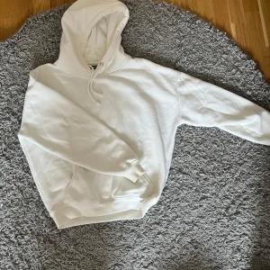 Vit hoodie från Bik Bok - Säljer en klassisk vit hoodie från Bik Bok i storlek XS. Tröjan har huva med dragsko och en stor magficka framtill. Perfekt för en avslappnad och stilren look.