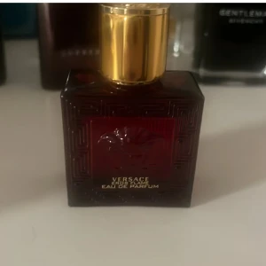 Versace Eros Flame Eau de Parfum - Versace Eros Flame Eau de Parfum för herr, i en mörkröd fyrkantig glasflaska med guldigt lock. Flaskan har ett elegant mönster och Versaces ikoniska Medusa-huvud på framsidan. En lyxig och intensiv doft.