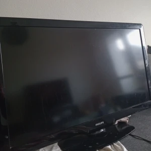 Svart TV från Philips - Säljer en svart platt-TV från Philips med bred ram och klassisk design. Perfekt för vardagsrummet eller sovrummet. Står på en stabil fot och har en stilren look som passar in i de flesta hem.