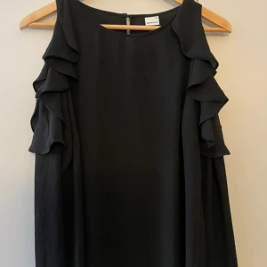Svart tröja från Gina Tricot - Säljer en svart tröja från Gina Tricot i storlek 36, med öppna axlar. Tröjan har ärmlös design med öppna axlar och en rak, lös passform. Använd nån enstaka gång, men är som ny. 