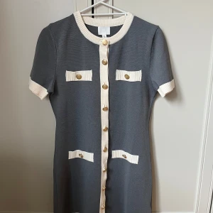 Grå klänning med guldknappar från H&M - Snygg grå klänning från H&M med vita ribbade kanter och guldknappar framtill. Klänningen har korta ärmar och dekorativa fickor på bröstet och höfterna. Perfekt för en stilren look. Den är toppmodern och i nyskick. Hittar inga skavanker alls, ej noppig eller fläckig. Nypriset är 400 kr. Mitt pris: 150 kr. . 