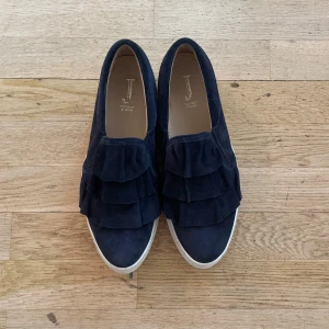 Marinblå sneakers med volanger - Säljer ett par marinblå sneakers i mocka från J. Shoes med volangdetaljer framtill. Fina både som vardagskor och vid mer uppklädda tillfällen!💕