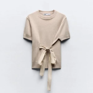 Beige stickad topp med knyt från Zara - Säljer en beige stickad topp från Zara med korta ärmar och snygg knytning i midjan. Tröjan har rund halsringning och ribbade detaljer vid ärmslut och nederkant. Perfekt för en stilren och trendig look.