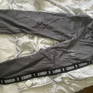 Svarta mjukisbyxor från Hoodrich - Säljer ett par mörkgrå träningsbyxor från Hoodrich i storlek L. Byxorna har resår i midjan och ett svart band längs benen med Hoodrich-loggan tryckt i vitt. Perfekta för en avslappnad stil. Slitage finns vid texten (se bild 3)