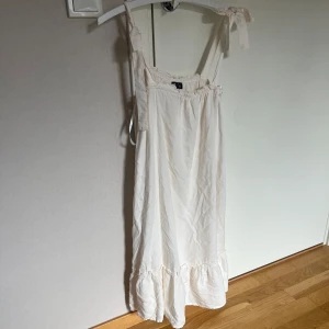 Vit kortklänning med volang från Pieces - Säljer en söt vit kortklänning från Pieces med volang nertill och knytbara axelband.🩷