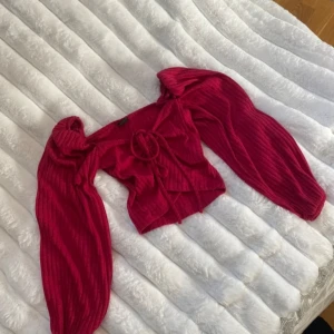 Ribbad röd rosa croppad topp från Gina Tricot - Säljer en snygg ribbad röd croppad topp från Gina Tricot. Toppen har långa ärmar, knytning framtill och är tillverkad i mjuk polyester. Perfekt för att lyfta din outfit med en färgklick!