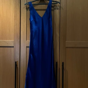 Blå långklänning i satin från Lindex - Säljer en elegant blå långklänning från Lindex i glansigt satinmaterial. Klänningen har v-ringning och är ärmlös, vilket ger en stilren och modern look💙