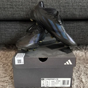 Adidas X Crazyfast.1 FG fotbollsskor - Säljer ett par svarta Adidas X Crazyfast.1 FG fotbollsskor i nästintill nyskick. Med blå detaljer och de tre klassiska ränderna på sidorna. Skorna har snörning och är tillverkade i syntetmaterial, perfekta för spel på både gräs och konstgräs. Nypris 2 999 kr