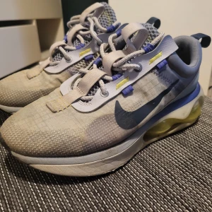Nike Air Max sneakers i grått och blått - Säljer ett par Nike Air Max sneakers i grå och blå färg med gula detaljer. Skorna har en synlig Air Max-bubbla i sulan, mesh- och syntetmaterial samt snörning. Perfekta för dig som gillar sportig stil och komfort.