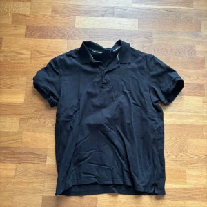 Svart pikétröja - Säljer en klassisk svart pikétröja med krage och knappar framtill. Perfekt för en clean och stilren look. Passar till det mesta och är enkel att matcha med andra plagg.