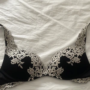 Svart och vit spets-bh från Intimissimi - Snygg svart bh från Intimissimi med vit spetsdetalj vid axelbanden. Bh:n har vackert blommönster i spetsen och justerbara band. 
