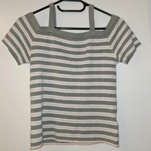 Randig ribbad topp med breda axelband - Säljer en söt randig topp med breda axelband och korta ärmar. Färgerna är ljusgrön, vit och ljusrosa, och materialet är ribbad bomull som ger en skön och mjuk känsla. Perfekt för dig som gillar en chill och stilren look.