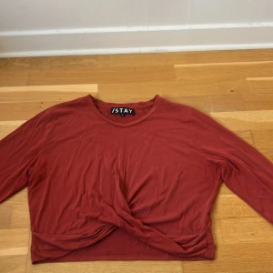 Röd croppad tröja från ISTAY - Säljer en röd långärmad tröja från STAY i storlek XL. Tröjan har en croppad passform och snygg twistad detalj framtill. Materialet känns mjukt och lätt, perfekt för dig som gillar enkel stil med en liten twist. Rund halsringning och slät yta.