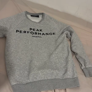Grå sweatshirt från Peak Performance - Snygg grå sweatshirt från Peak Performance med svart logotyptryck framtill. Klassisk rund halsringning, ribbade muddar och mjukt material som känns skönt mot huden. Oversized, går bra för många storlekar. Köpt för ungefär 1000kr💕pris går att diskutera