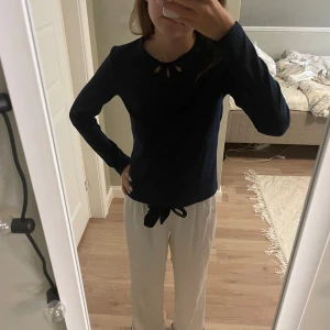 Mörkblå glittrig tröja från Lindex - Mörkblå långärmad tröja från Lindex med glittriga inslag och ribbad struktur. Snygg detalj med utskurna hål vid halsringningen som ger en unik look. Perfekt för dig som gillar lite extra bling i vardagen.