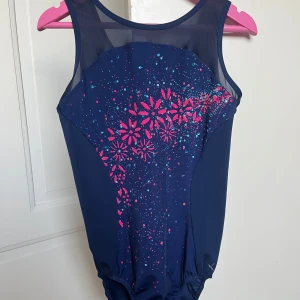 Marinblå gymnastikdräkt - Snygg marinblå gymnastikdräkt med färgglada blommor i rosa och blått framtill. Dräkten är ärmlös och har elastisk nederkant för perfekt passform. Den är har skönare kanter än vad gymnastikdräkter brukar ha vilket är skönt att träna i. Passar i åldrar mellan 10-13 år skulle jag säga! Bara att skriva om ni är intresserade så kollar jag mått osv :)