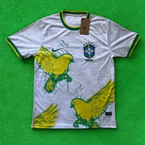 Vit Brasil Nike fotbollströja med tryck - Snygg vit Brasilien fotbollströja från Nike med gröna och gula detaljer. Stort gult fågeltryck framtill, grönt och gult kantband vid hals och ärmslut. Broderat Brasilien-emblem på bröstet och Nike-logga. Tillverkad i lätt och ventilerande material.